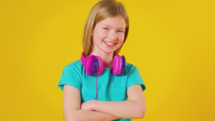 工作室拍摄的女孩戴着耳机微笑着看着黄色工作室背景下的相机-慢动作拍摄