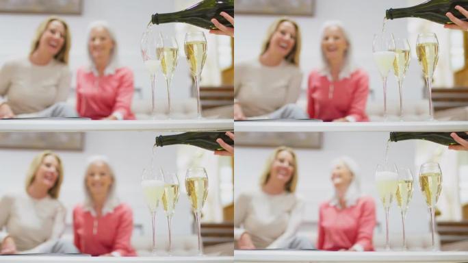普罗塞克或香槟被倒入玻璃杯中的特写镜头，两名妇女坐在沙发上，背景是慢动作拍摄
