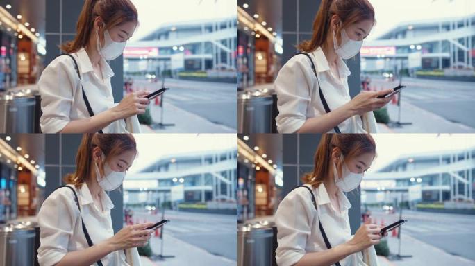 年轻的亚洲女商人穿着时尚的办公室衣服，戴着医用口罩，在城市现代城市中坐在户外时使用智能手机打字短信。