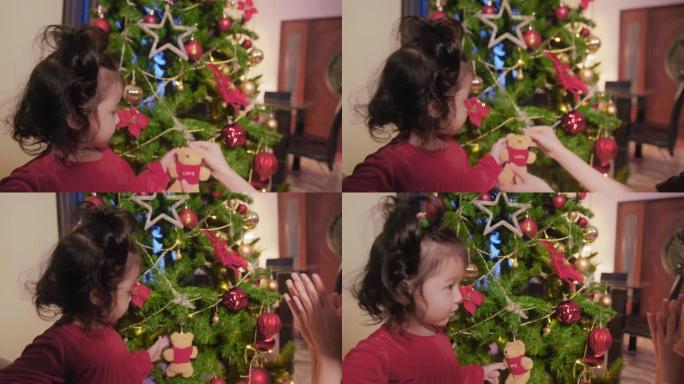 亚洲蹒跚学步的女孩喜欢在家装饰圣诞树。可爱的小女儿和她的12月假期玩得开心。