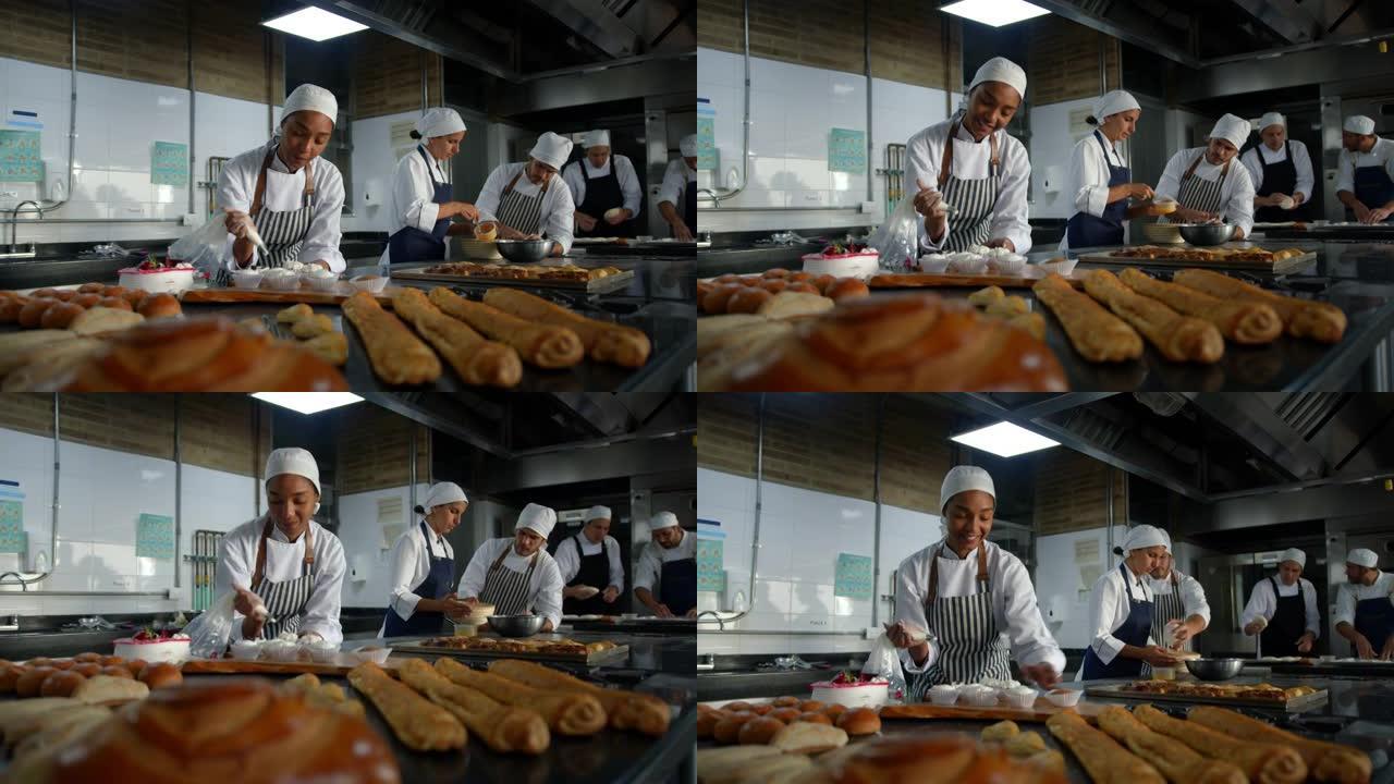 忙碌的面包师团队在一家面包店成对工作，而快乐的黑人女性面包师则用白色糖霜装饰纸杯蛋糕