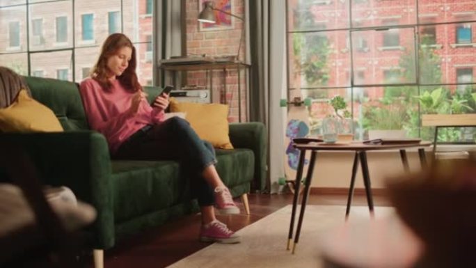 年轻漂亮的女性坐在客厅的沙发上，放松并使用智能手机。创意女孩检查社交媒体，与朋友聊天，浏览互联网。从