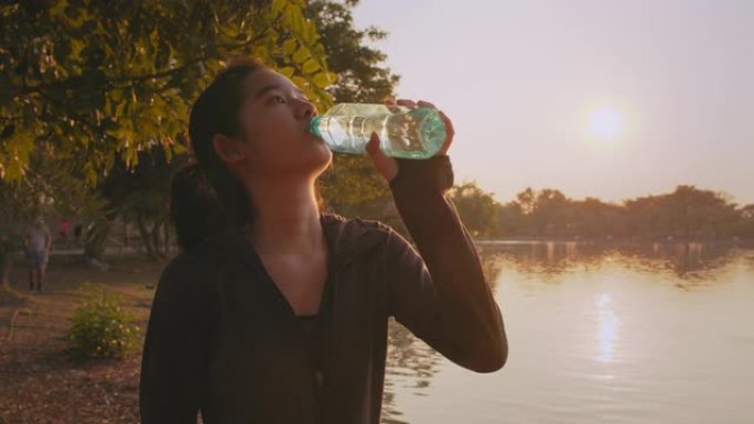 迷人的亚洲少女跑步后喝水在公园补水