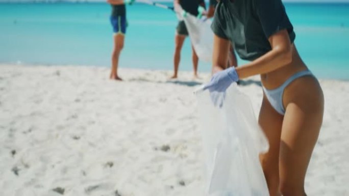 一组年轻志愿者的慢动作在阳光明媚的日子里在大海的海滩上捡拾塑料垃圾，以保护环境。
