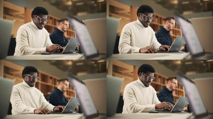 热情的黑人打开笔记本电脑并在办公室开始工作的肖像。男平面设计师在开发新的视觉概念时微笑着。手持镜头