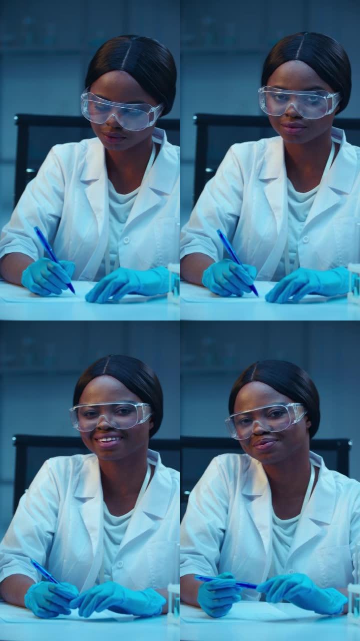 一位迷人的非裔美国医生微笑着看着相机，坐在现代实验室的工作场所
