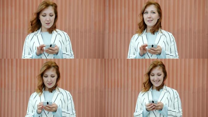 快乐的红发女人的肖像使用智能手机微笑站在户外
