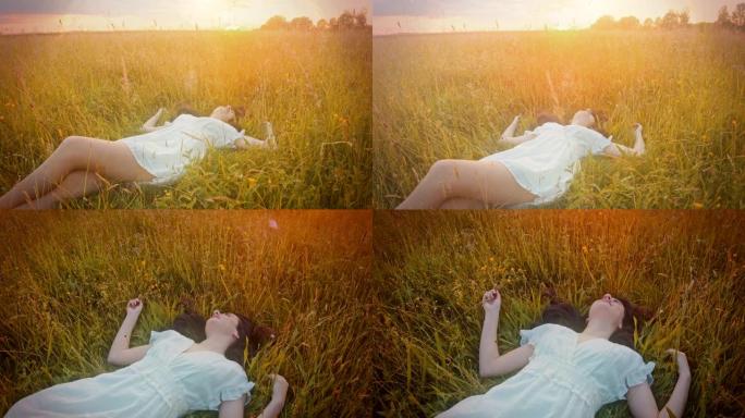 日落时分，穿着白色连衣裙的SLO MO美丽的年轻女子躺在草地上