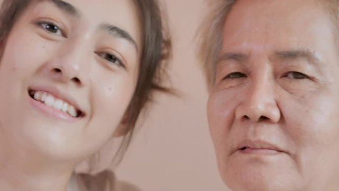 特写，肖像快乐志愿者亚洲年轻女性看守人与亚洲老年母亲病人在家里看相机。家庭工作室