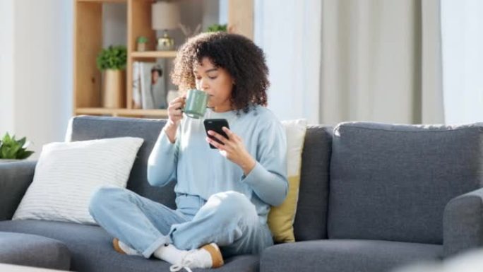 女人在家里喝咖啡时在手机上阅读短信，在线浏览社交媒体或浏览应用程序。一位快乐，微笑和舒适的黑人女性喝