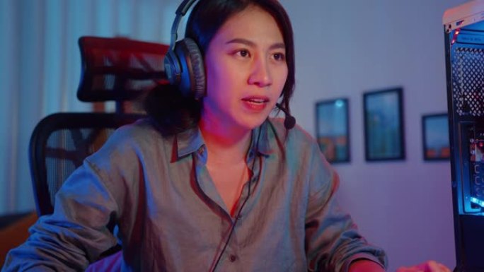 快乐亚洲职业女孩游戏玩家戴着耳机参与在家客厅玩视频游戏彩色霓虹灯电脑。