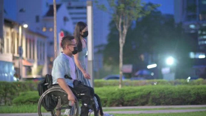 旅游亚洲华裔男子坐轮椅晚上在城市街与他的女性朋友交谈