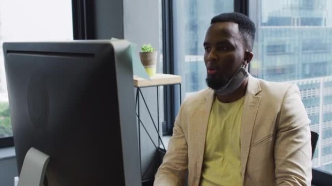非裔美国人在mode坐在办公桌上时，脖子上戴着口罩，用电脑