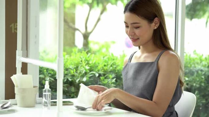 亚洲妇女在新的普通餐厅用餐前用酒精清洗餐具