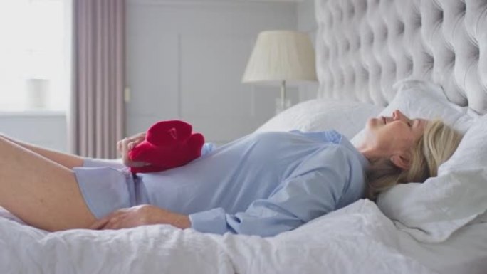 更年期成熟的女人躺在家里的床上拿着热水瓶-慢动作拍摄