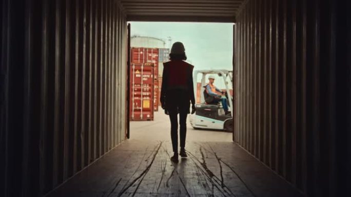 女工业主管和安全检查员走出物流作业港口码头的一个运输货物集装箱。叉车司机驾驶通行证，带箱子装载托盘。