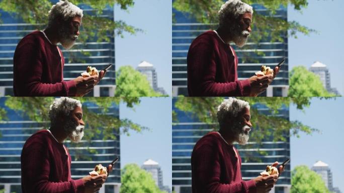 非裔美国人高级男子在公司公园吃零食并使用智能手机