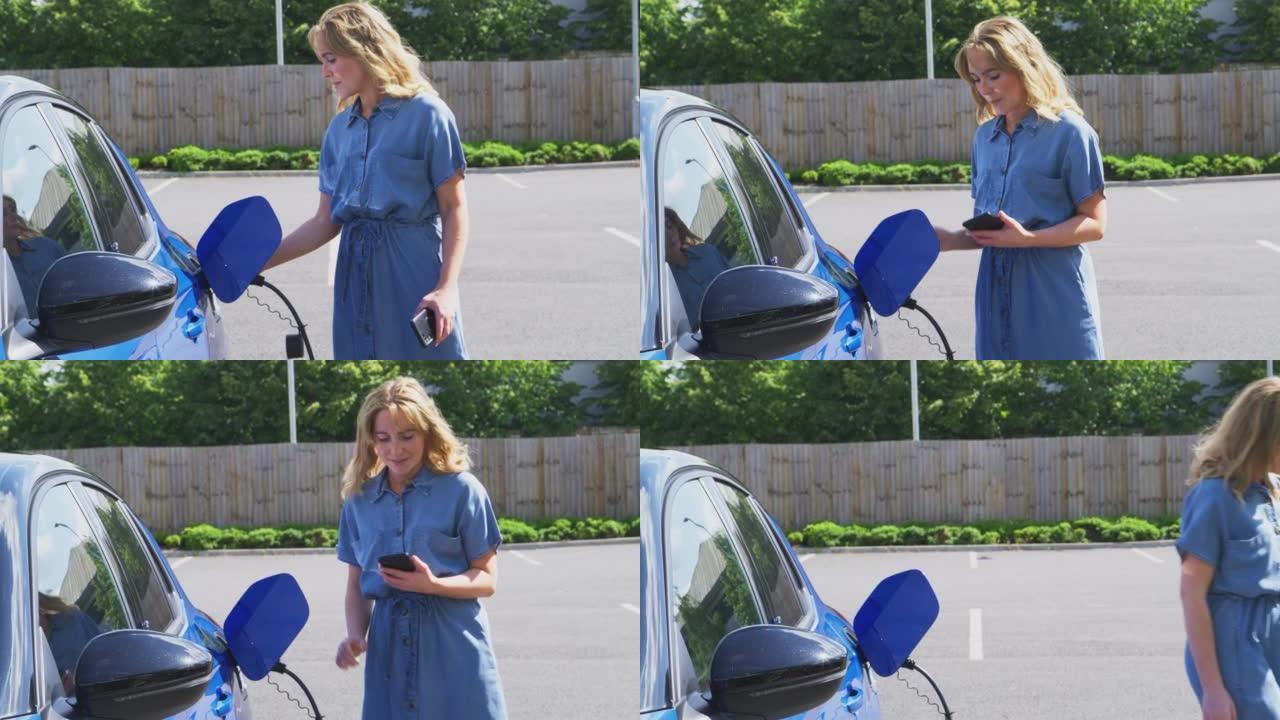女人在户外充电站使用手机上的应用程序检查电动汽车的电池电量-慢动作拍摄