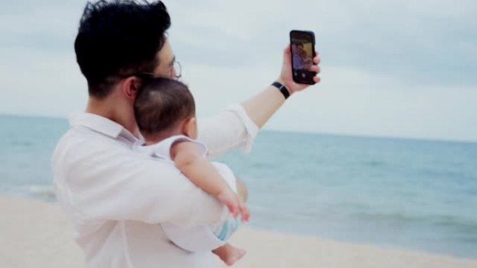 周末在海滩上旅行时，父亲抱着新生婴儿并使用手机自拍