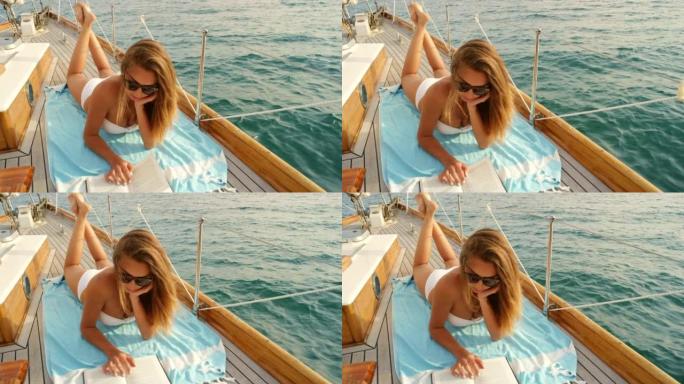 穿着白色比基尼的年轻女子在意大利海岸航行的游艇上放松和看书。在意大利巡游期间，放松的年轻女子躺在游艇