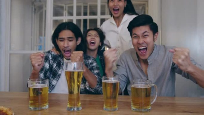 一群年轻的亚洲游客朋友在体育电视上看足球，喝酒精啤酒，并在考山路的夜总会举行聚会。