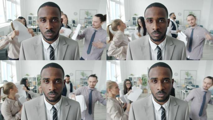 严肃的非洲裔美国企业家站在办公室，团队跳舞时玩得开心的慢动作肖像