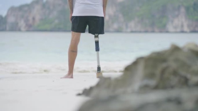 早上在海滩上做伸展运动的假肢残疾人的后视图。残疾收藏: 日常生活概念。