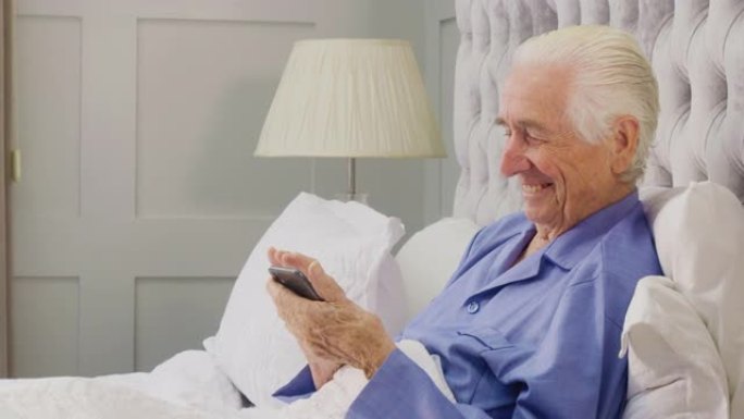 微笑的老人在家穿着睡衣躺在床上用手机