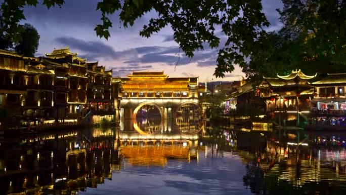 凤凰，中国。明亮的灯光照明的夜晚景观。沱江上的桥梁倒影。人们玩得很开心。平移镜头，UHD