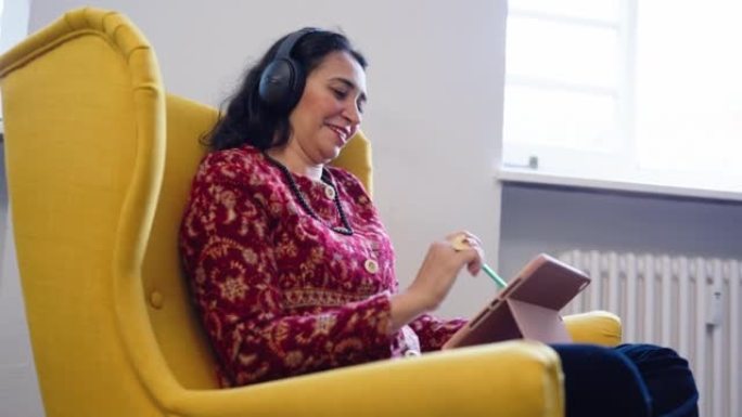 中东女商人，戴着耳机，坐在扶手椅上的数字平板电脑