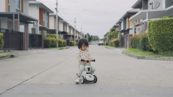 快乐的亚洲小女孩骑着蹒跚学步的踏板车。