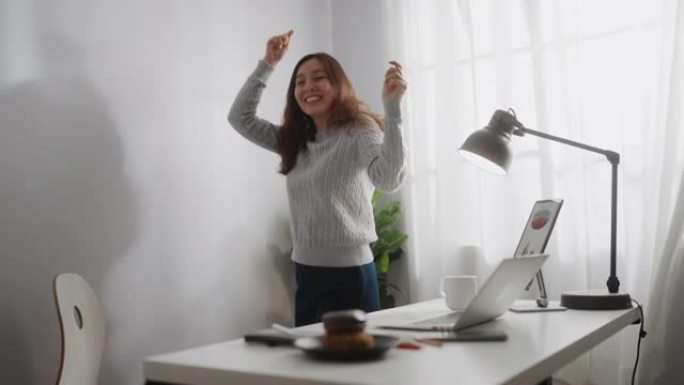 亚洲女子在家中使用笔记本电脑时跳舞