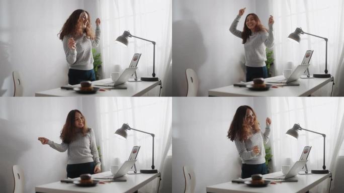 亚洲女子在家中使用笔记本电脑时跳舞