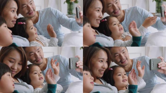 快乐的亚洲家庭在床上使用智能手机进行视频聊天母亲和父亲，孩子们在手机上挥舞着与朋友聊天，享受在线交流