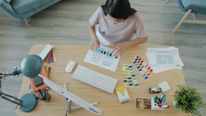 年轻的亚洲女士设计智能手机应用程序的高角度视图，选择在家工作的颜色