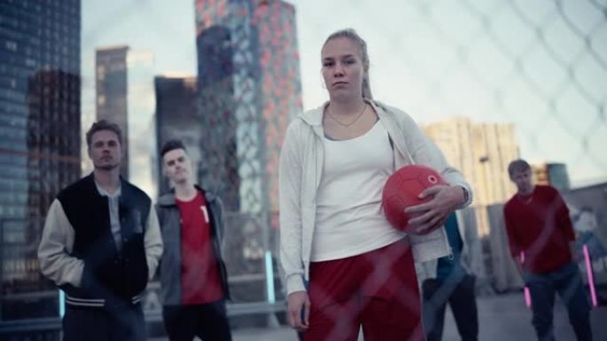 一个美丽的运动型年轻女子看着相机，手里拿着一个红色足球的肖像。时尚的女足球运动员与一群多元文化的人站
