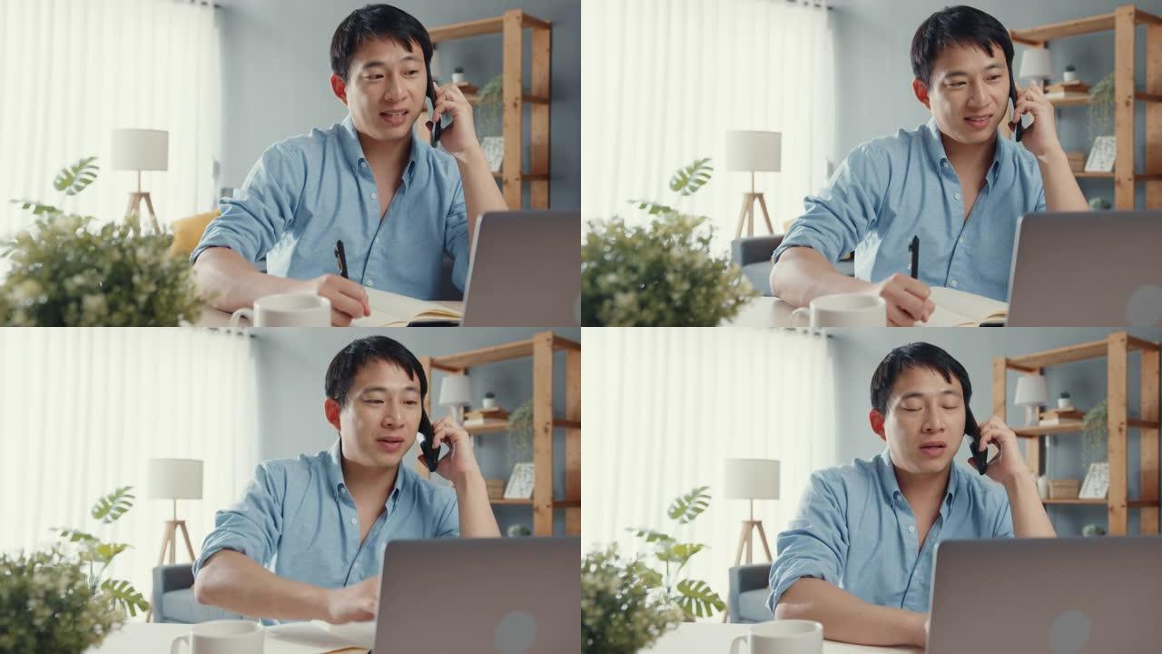 自由职业者亚洲男休闲服使用笔记本电脑在家里的客厅用手机通话。