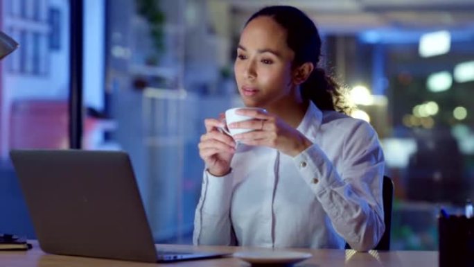 放松的女商人深夜在笔记本电脑上工作，一边看电子邮件，一边喝咖啡，一边看起来很满意。公司专业人员下班后