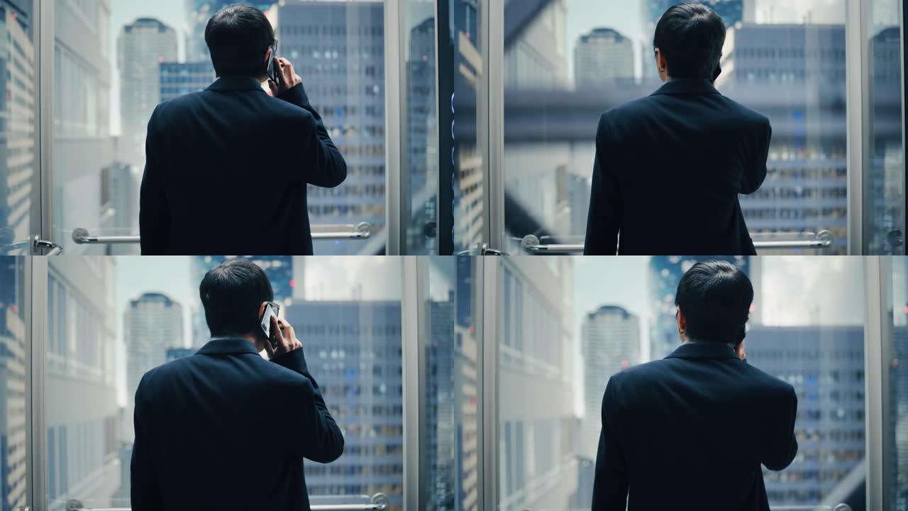 成功的时尚日本商人骑玻璃电梯到现代商务中心的办公室。英俊快乐的男人在打电话，在电梯里接一个重要的商务