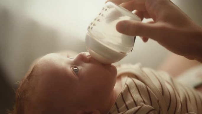 真实的特写镜头，一个新生儿躺在婴儿床的背上，从小婴儿奶瓶里喝牛奶。白人新生儿在家中的肖像。童年和父母