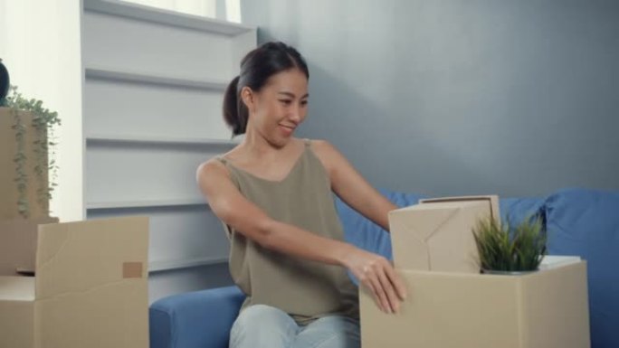 自己的房子。年轻迷人的快乐亚洲女人随意坐在长途汽车上享受开箱的房地产购买和搬到家里客厅的新家。公寓所
