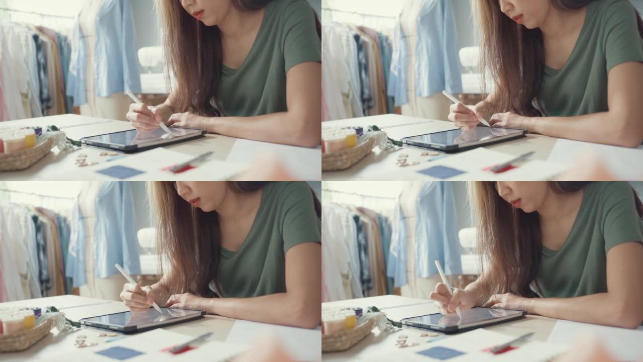 特写专业亚洲女性时装设计师与休闲使用数字平板电脑在她的商店创造新的系列。裁缝女士研究在大学工作室的平