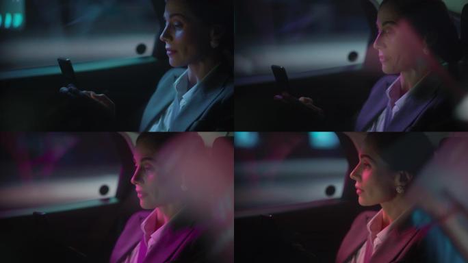 美丽的女商人晚上正坐在汽车后座上从办公室上下班。企业家在城市街道上使用智能手机，并在霓虹灯标志下转移