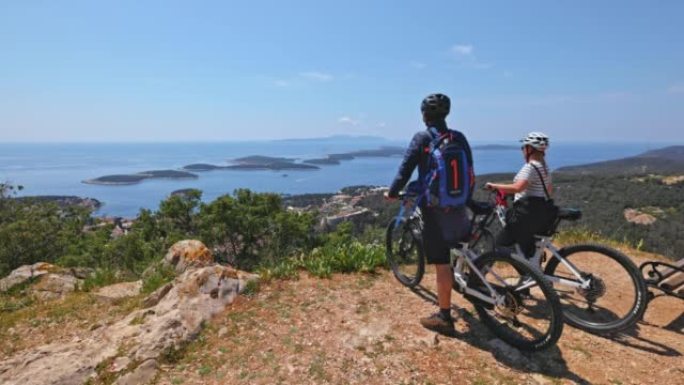 骑自行车的夫妇到达赫瓦尔岛的山顶，休息一下，聊天，看着风景
