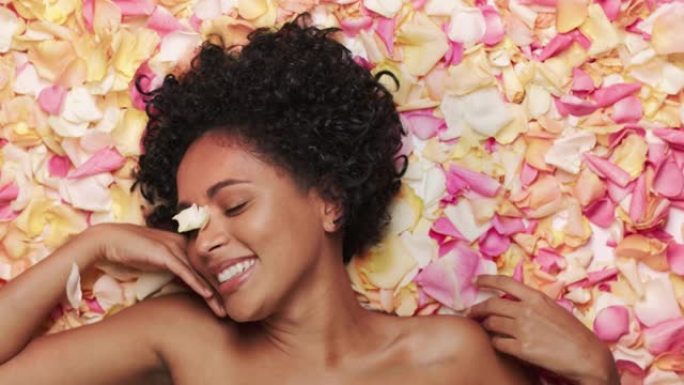 女性美女肖像躺在花坛上。性感的黑人多民族女性，有着非洲的头发，自然、干净、健康的皮肤摆姿势，微笑着。