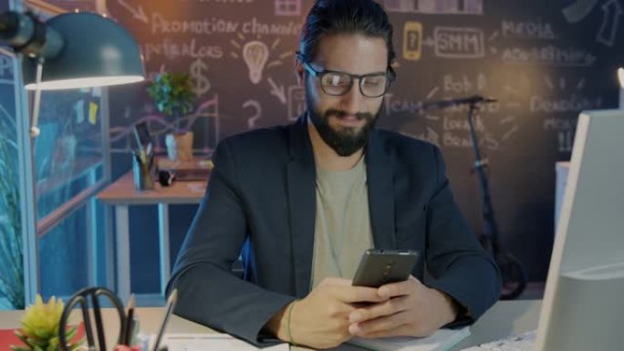 使用智能手机短信和微笑在办公室工作到很晚的成功企业家肖像