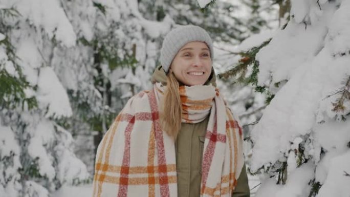 穿着冬装的年轻女士的肖像站在松树下的门下，随着雪的落下而笑