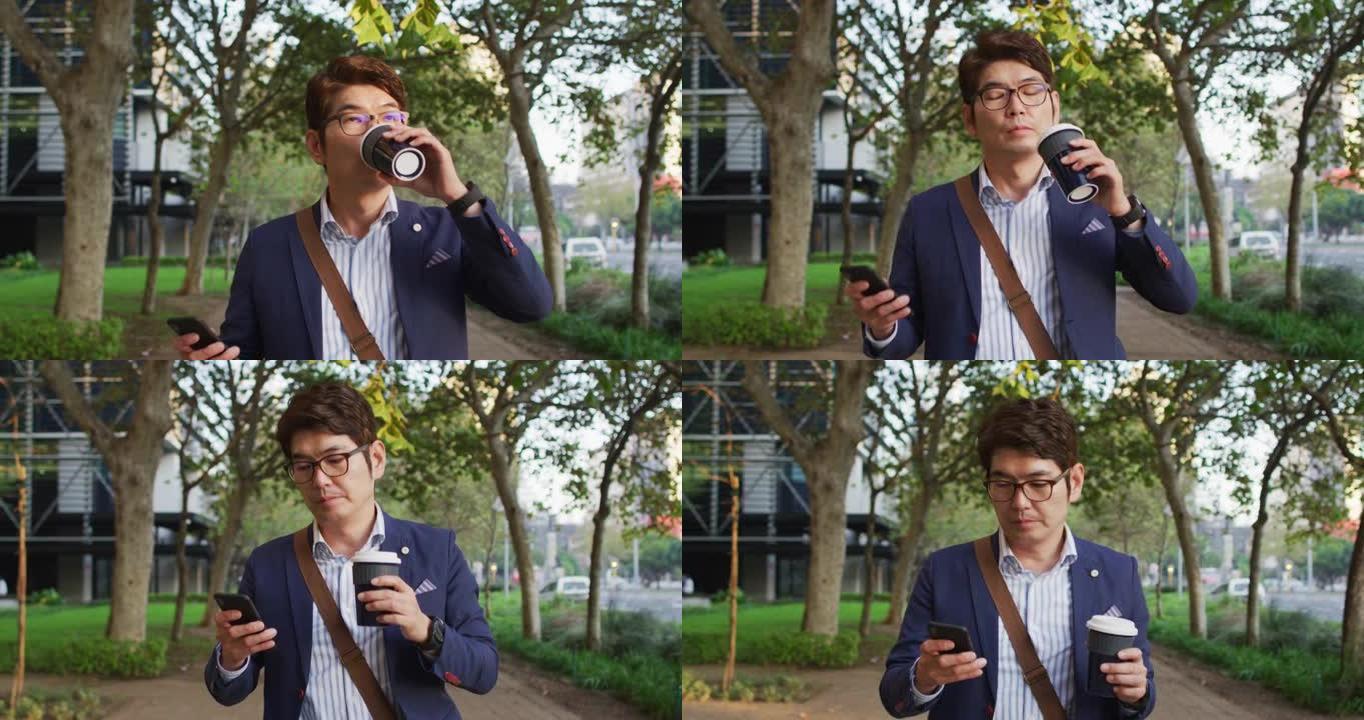 亚洲男子在公园散步时用智能手机拿着咖啡杯