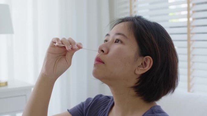 亚洲女性在家测试鼻covid冠状病毒快速自我拭子套件。