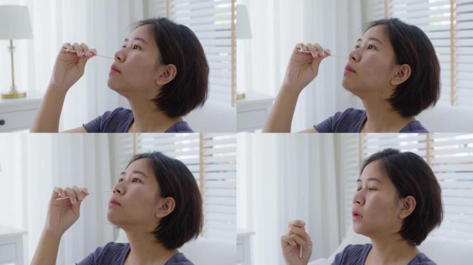 亚洲女性在家测试鼻covid冠状病毒快速自我拭子套件。